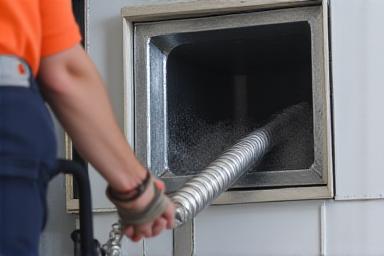 Technician extending a flexible hose into an air duct for cleaning